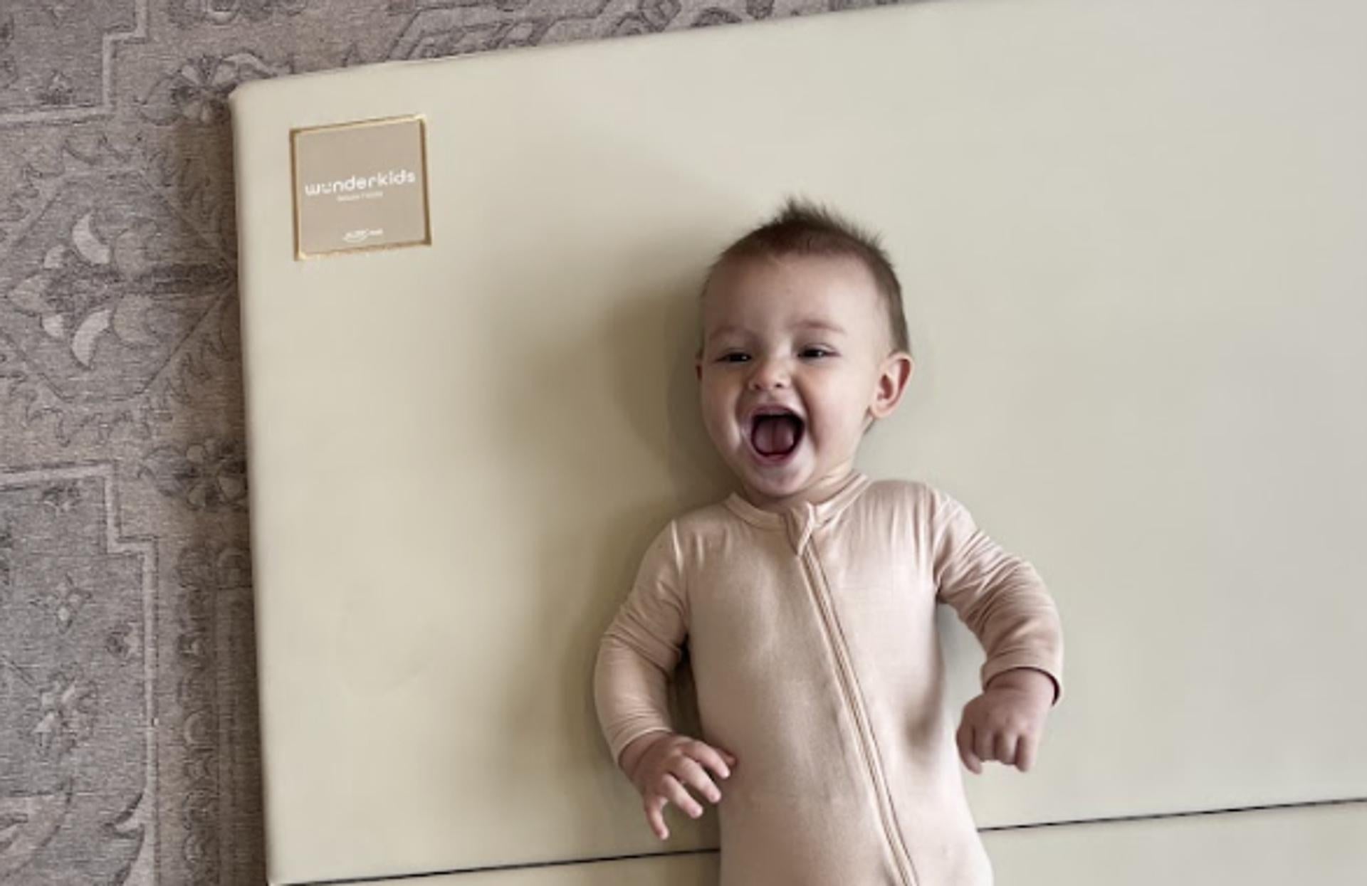 Newborn baby lying on a Wunderkids foldable play mat smililng