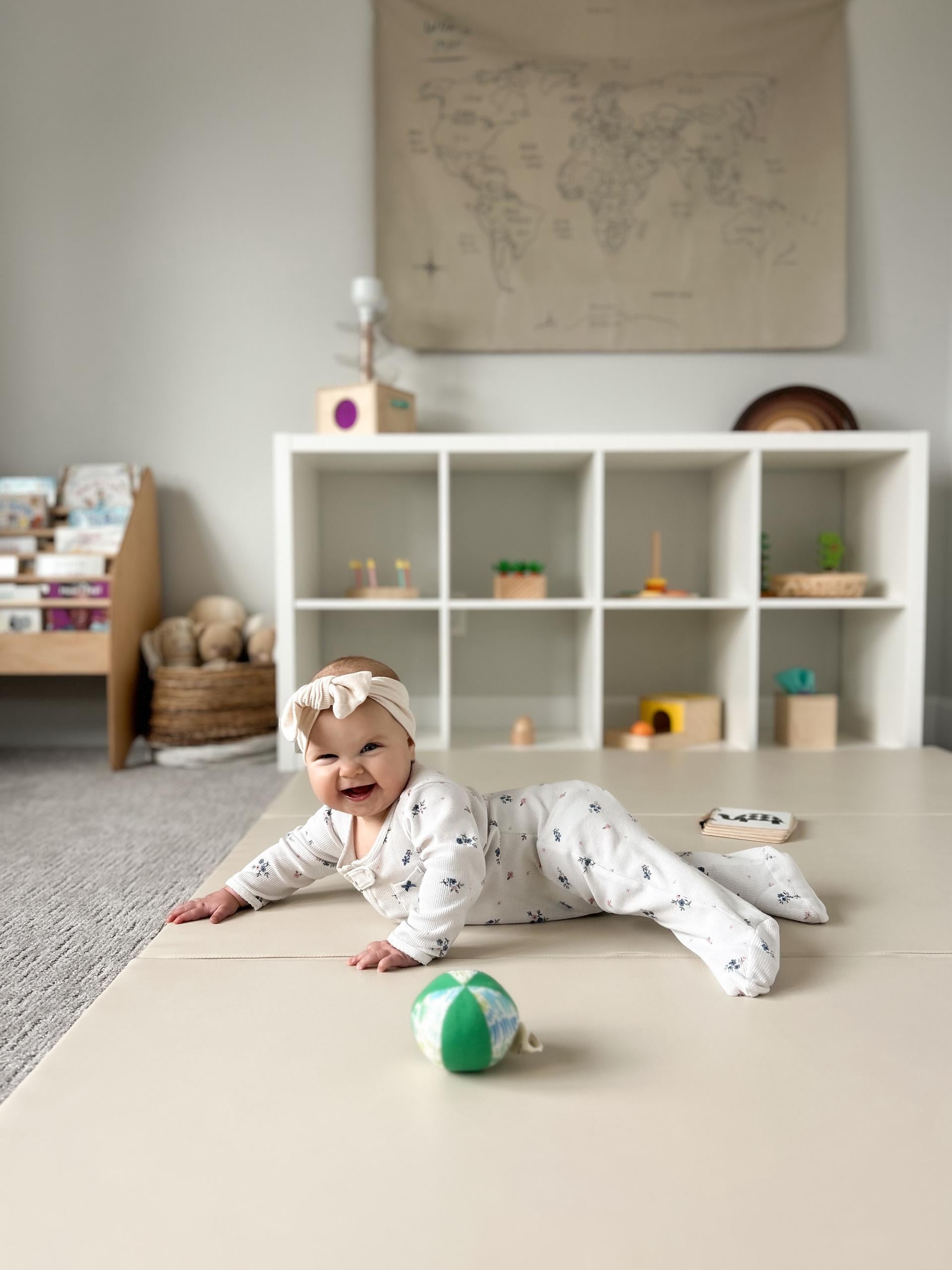 A smiling newborn baby enjoying tummy time on a Wunderkids play mat