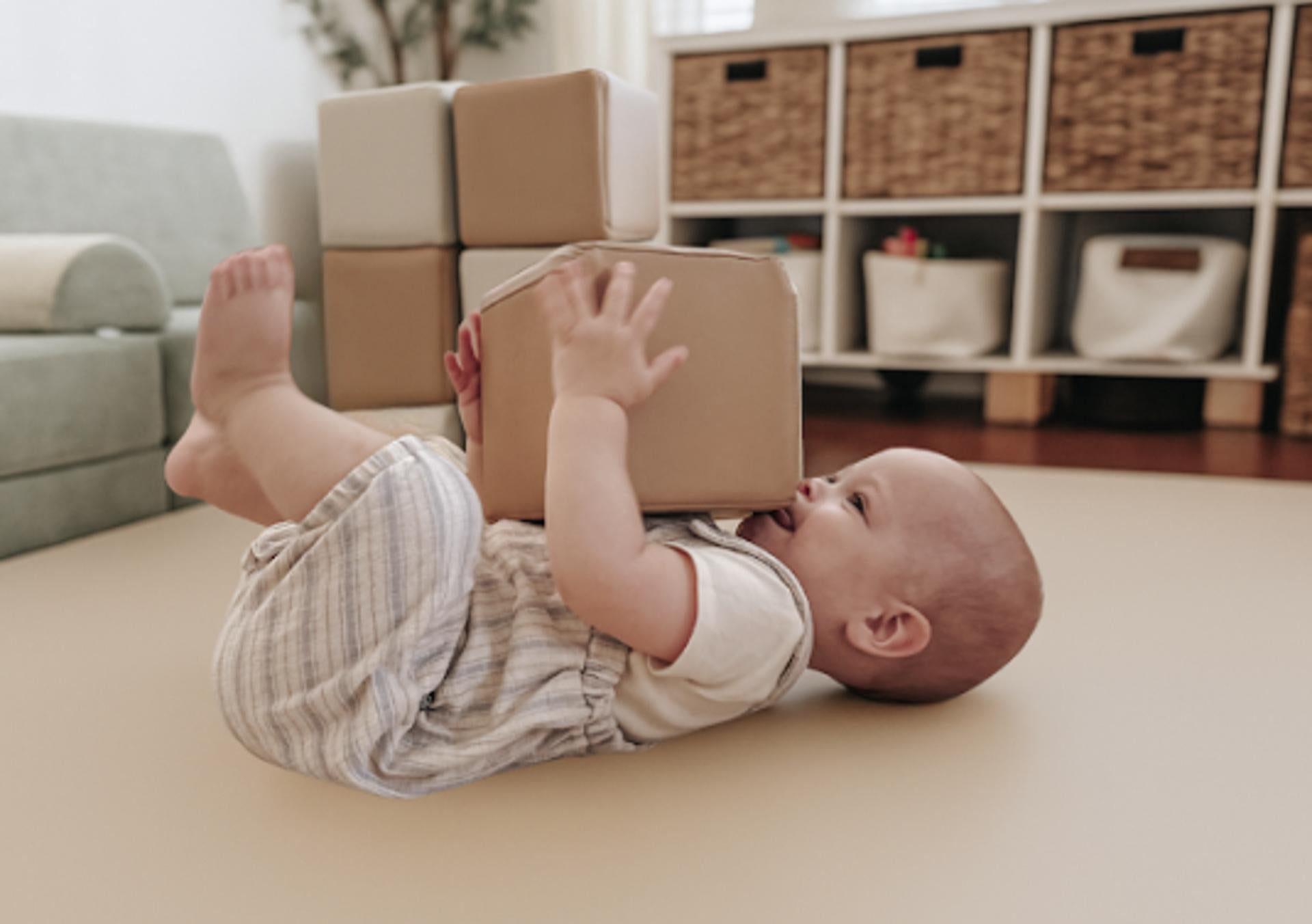 Baby on a padded play mat holding a foam block