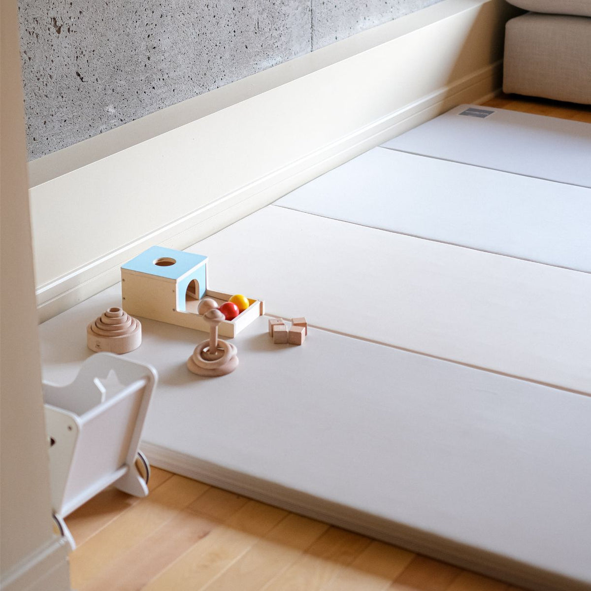 A child's wooden walker and two folded mats sit in a room corner with framed art.
